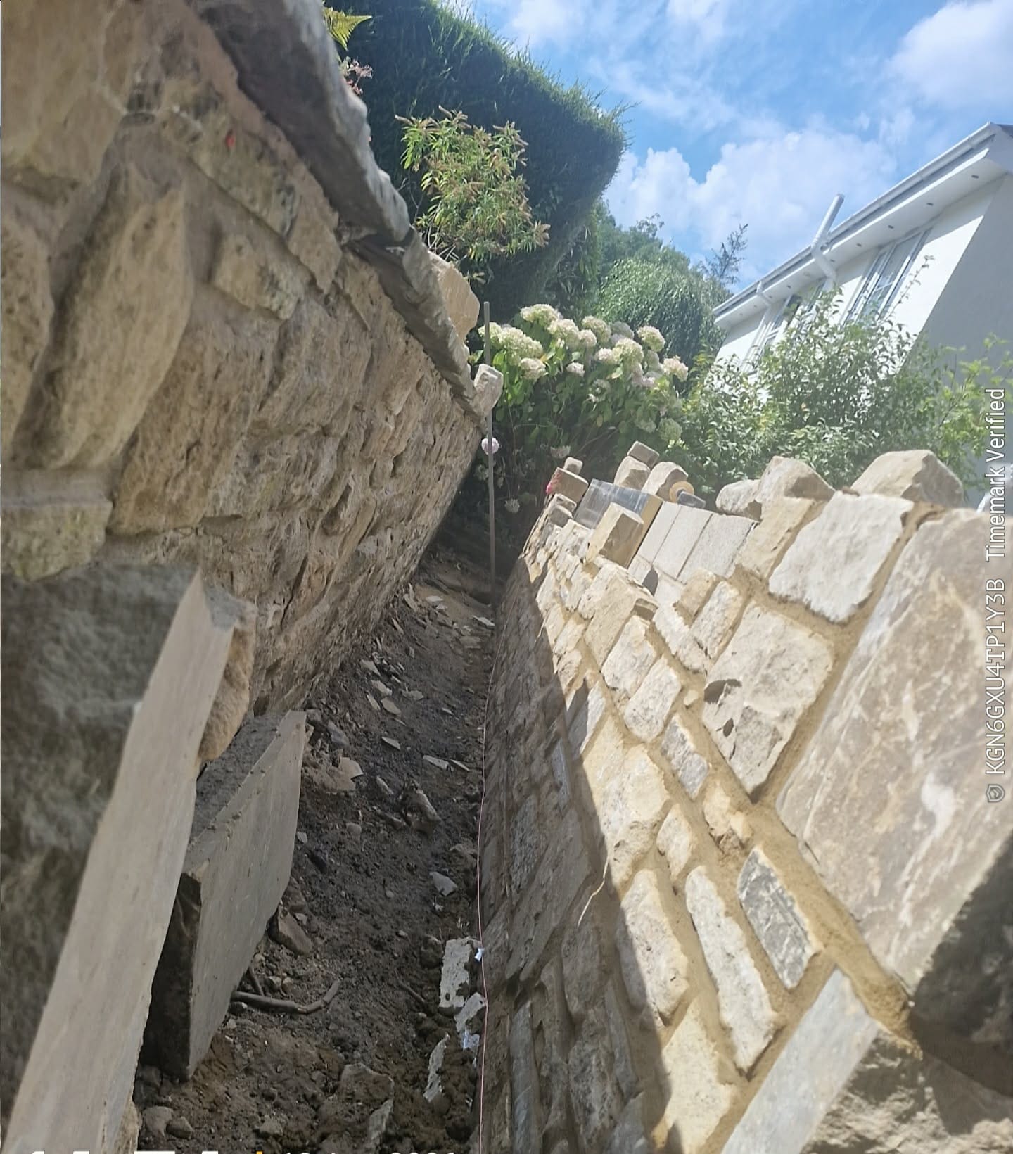 New natural stone garden wall being built alongside an existing stone boundary wall