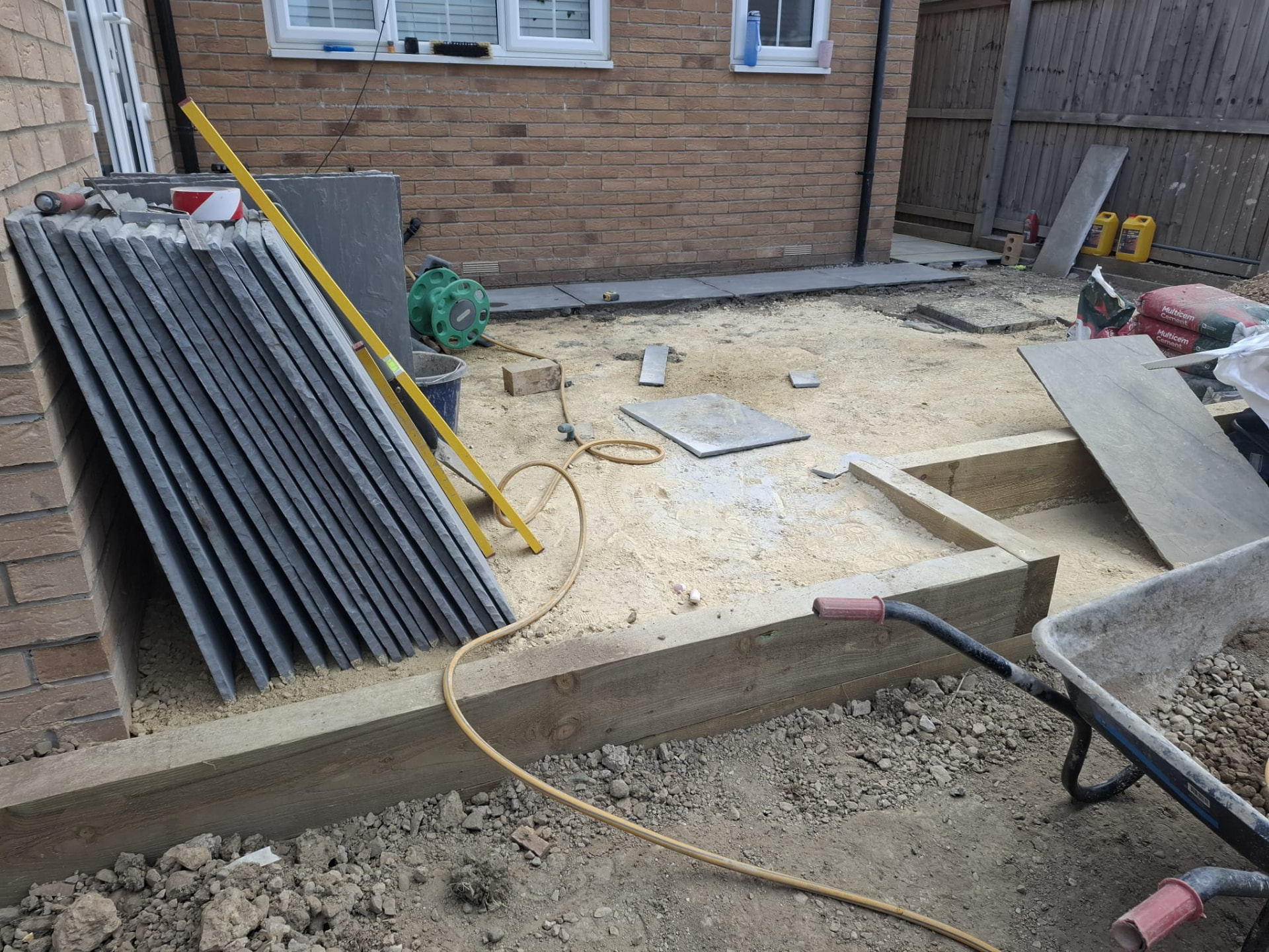Indian sandstone paving slabs stacked on a screeded bed with sleeper edging during a patio installation