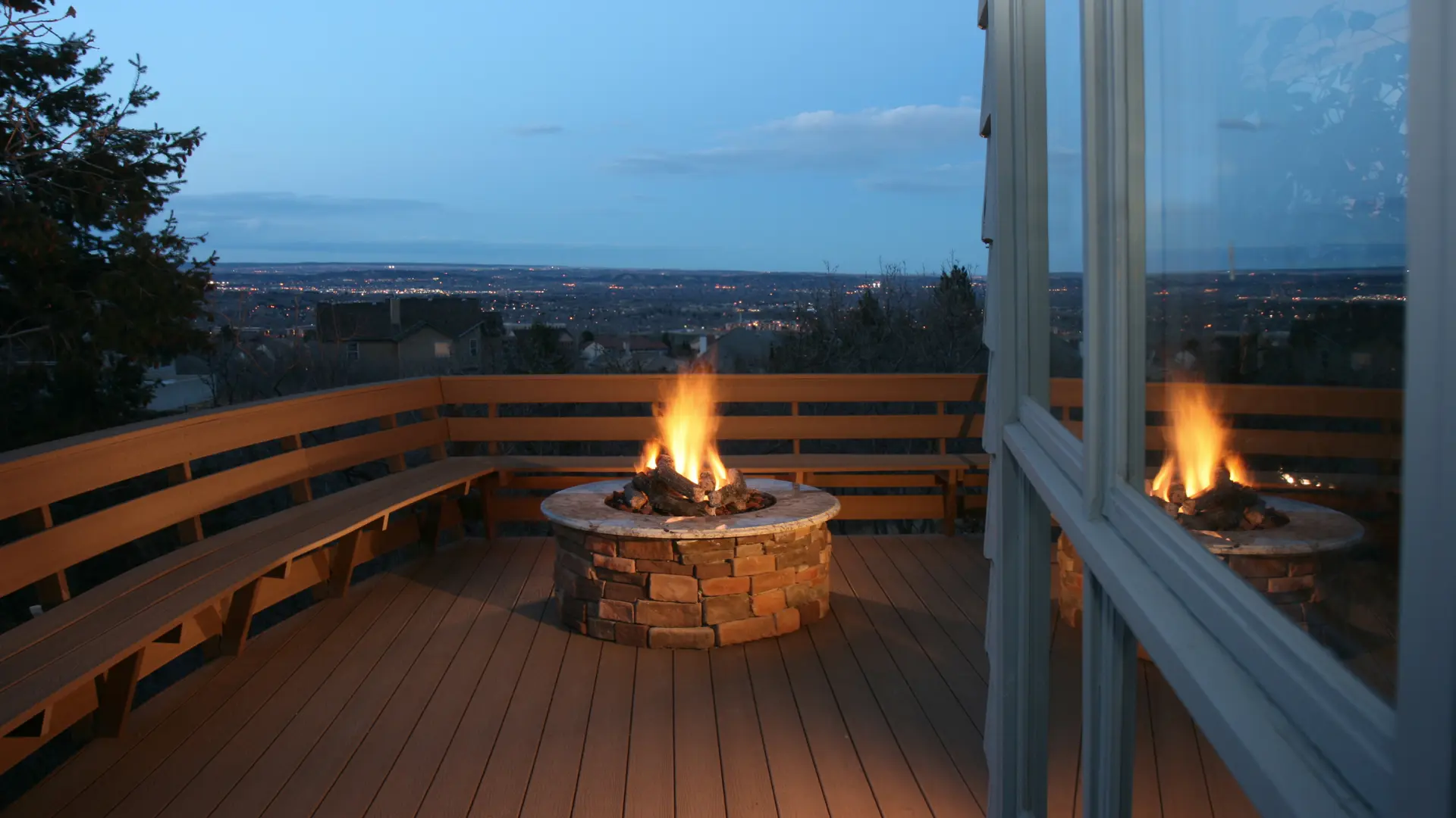Stone built firepit alight on a terrace with built-in bench seating at dusk