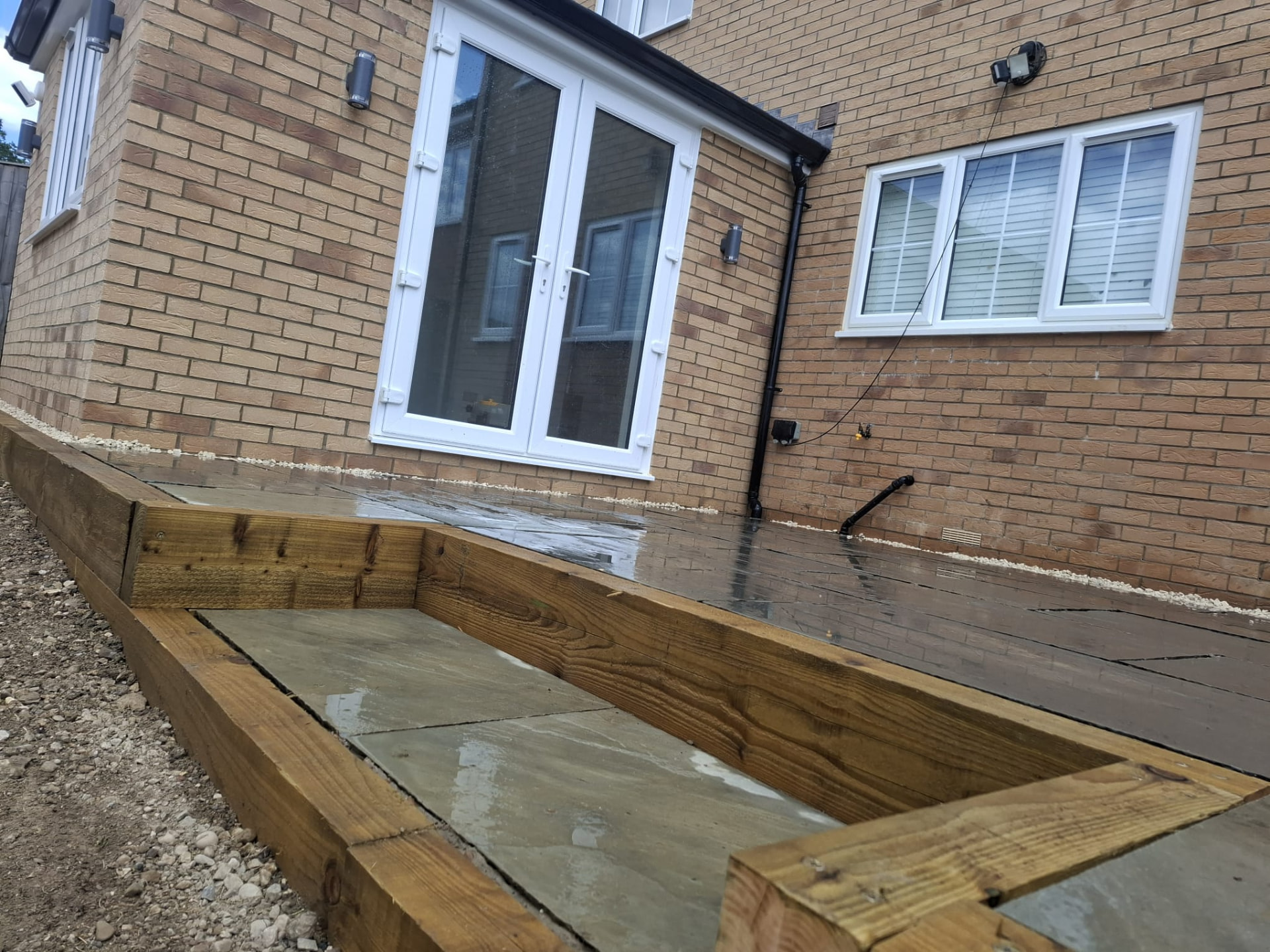 Sleeper-edged raised patio border and paving laid against the rear elevation of a house