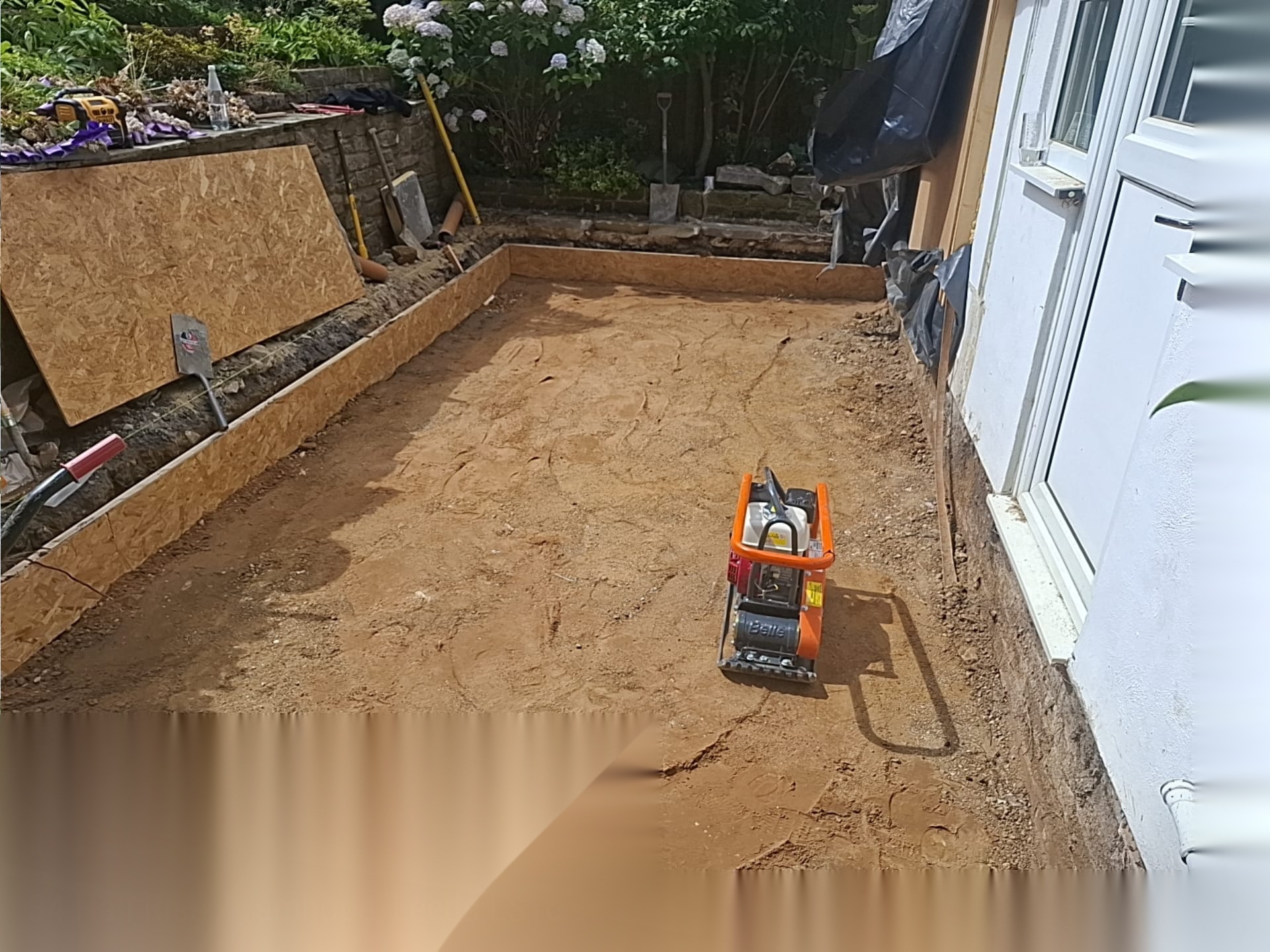 Sub-base compacted with a plate compactor across a prepared patio and foundation area