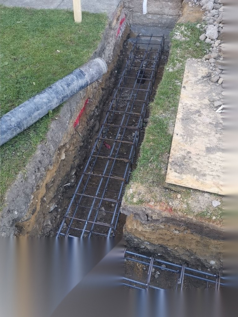 Steel reinforcement cage set in a foundation trench beside existing services before concrete is poured