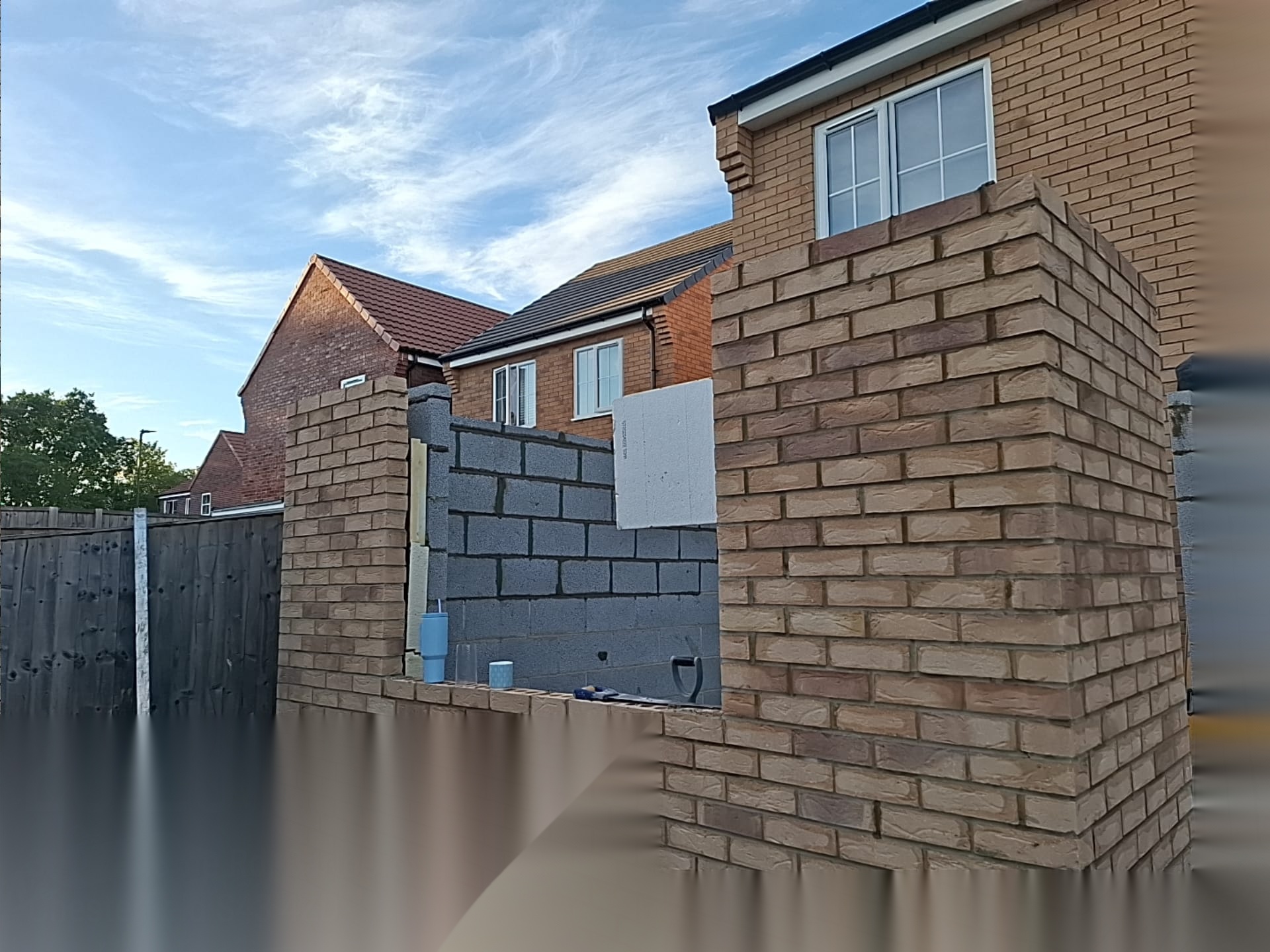 Brick entrance wall under construction over blockwork, showing the substructure beneath finished brickwork