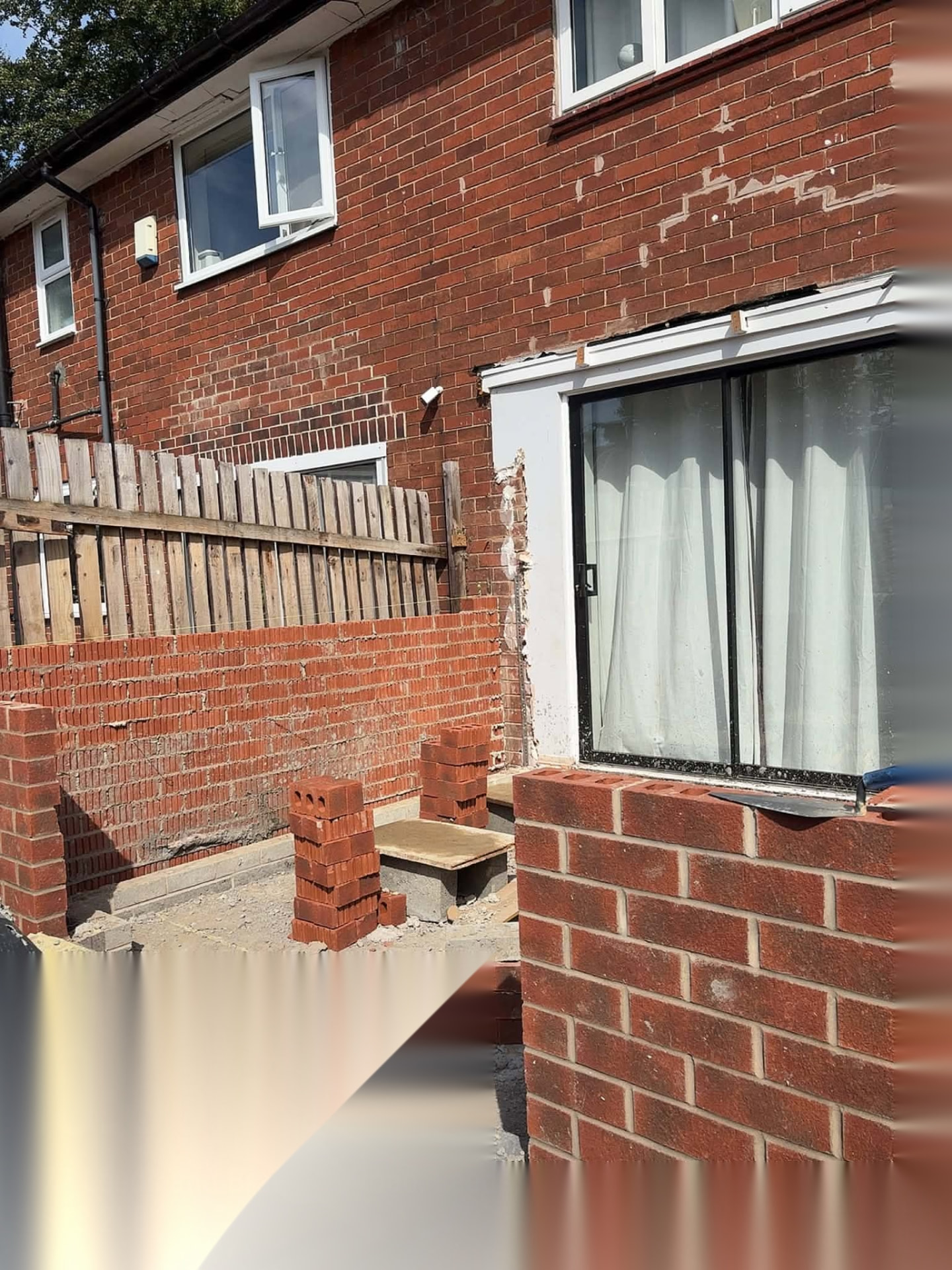 Red brick garden wall and house facade being repaired and repointed by a South Yorkshire bricklayer
