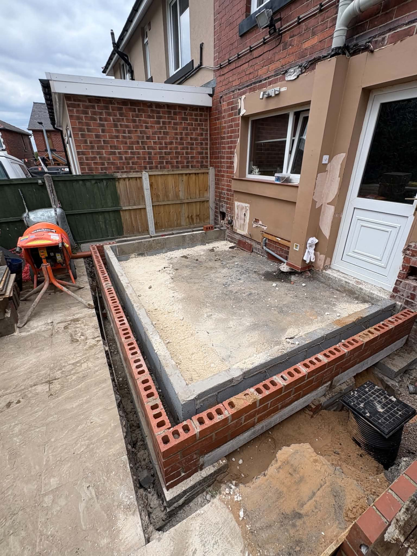 Red brick perimeter wall under construction beside a prepared patio base during a garden build