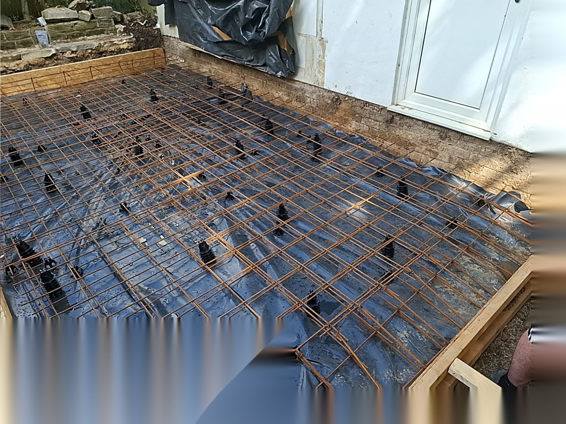 Reinforcement mesh over membrane against a house wall ready for a reinforced concrete slab