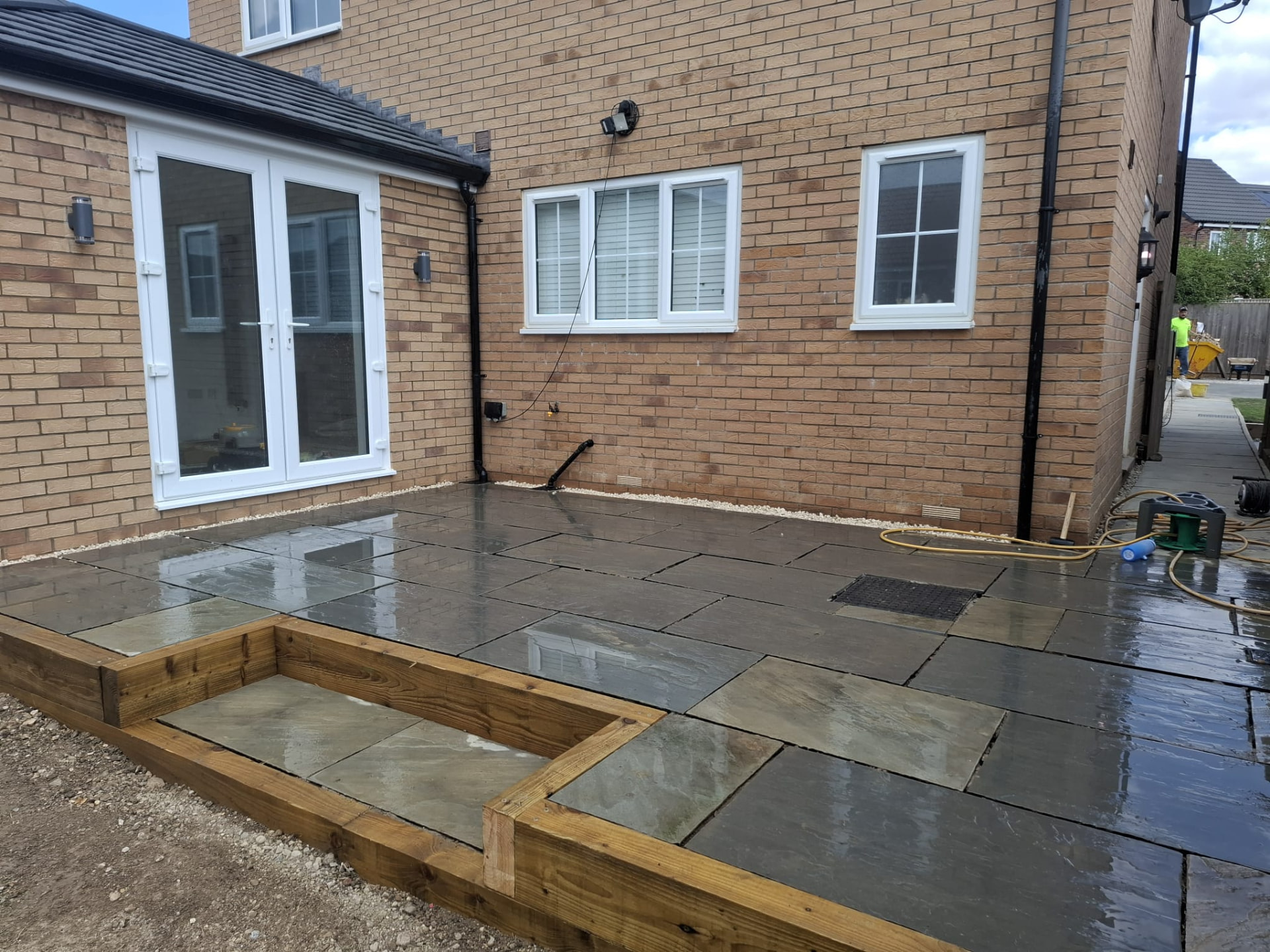 New grey sandstone patio laid true with a sleeper-edged planting bed beside French doors