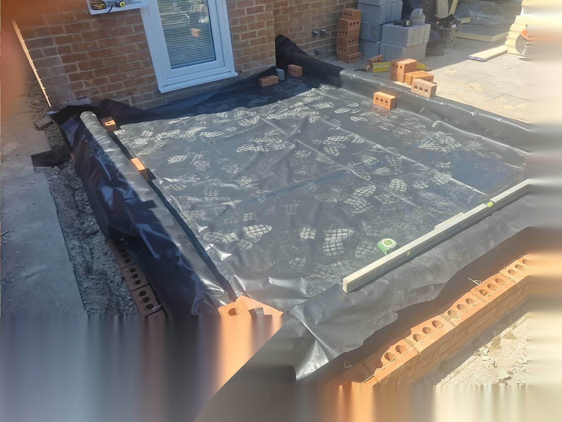 Membrane laid across a prepared area beside new brickwork with levels set out