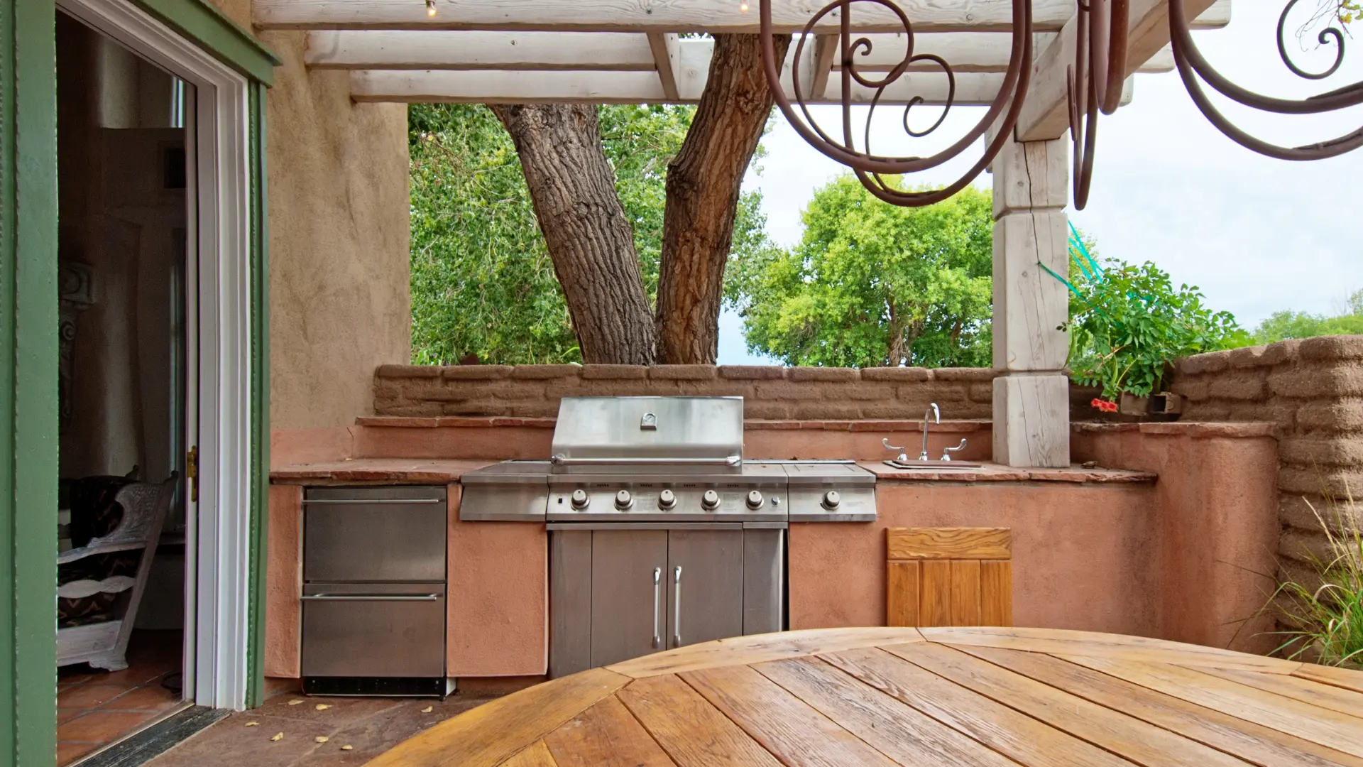 Built-in masonry outdoor kitchen with a barbecue, sink and rendered worktop under a covered terrace