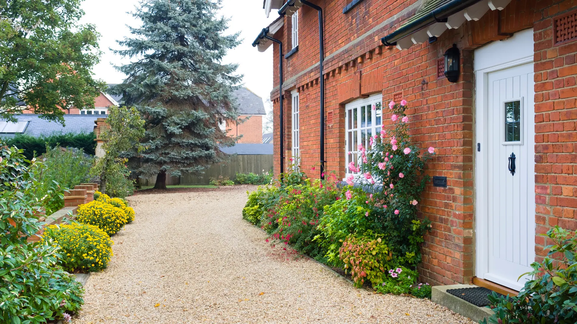 Bespoke garden design with a gravel path, brick edging and layered planting beside a red brick house