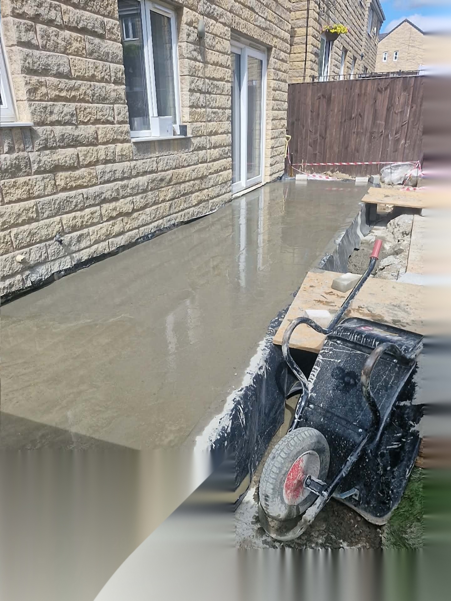 Freshly poured concrete path and slab set between shuttering beside a stone-faced house