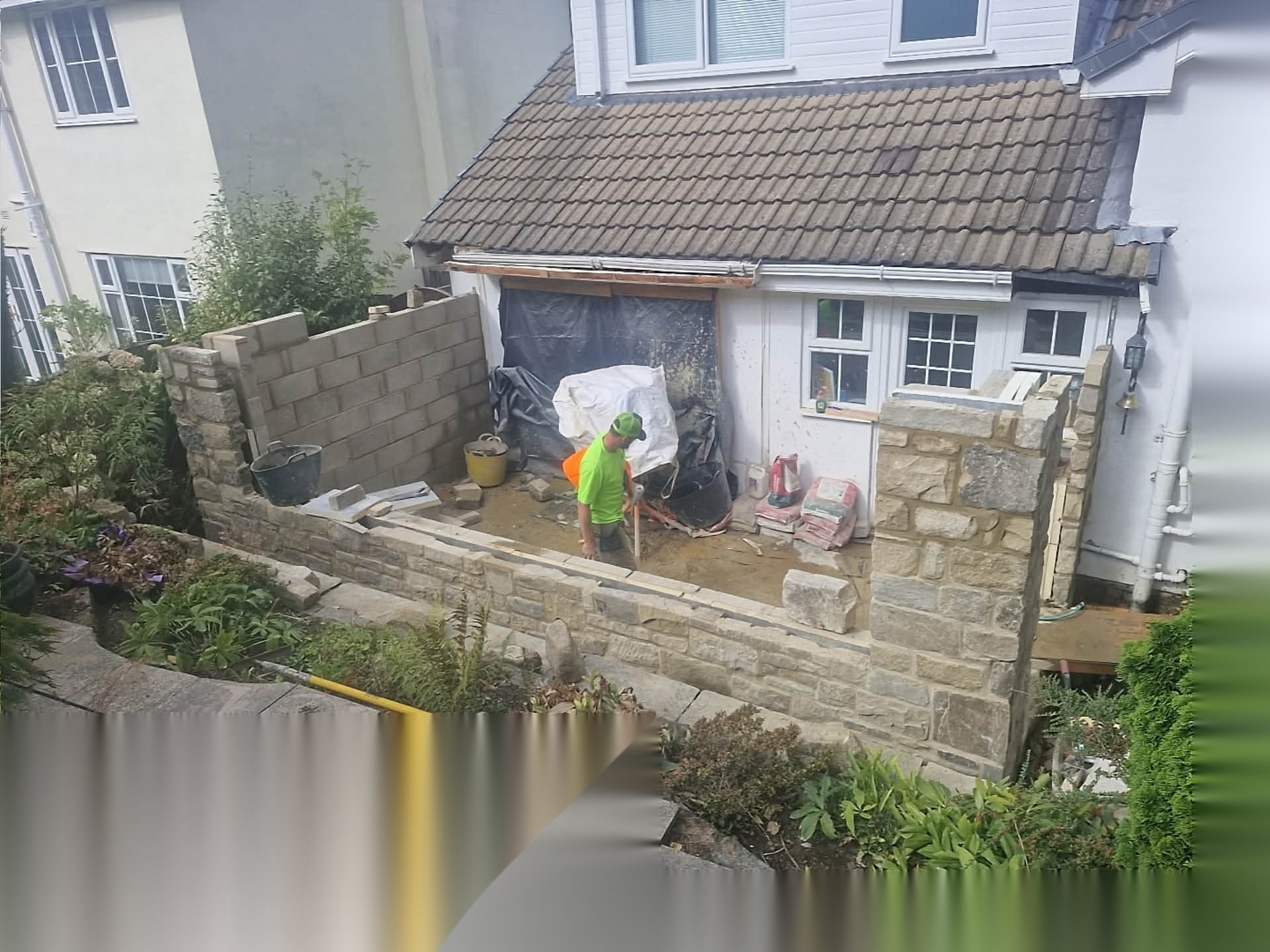 Stonemason building a coursed natural stone retaining wall around a sloping rear garden