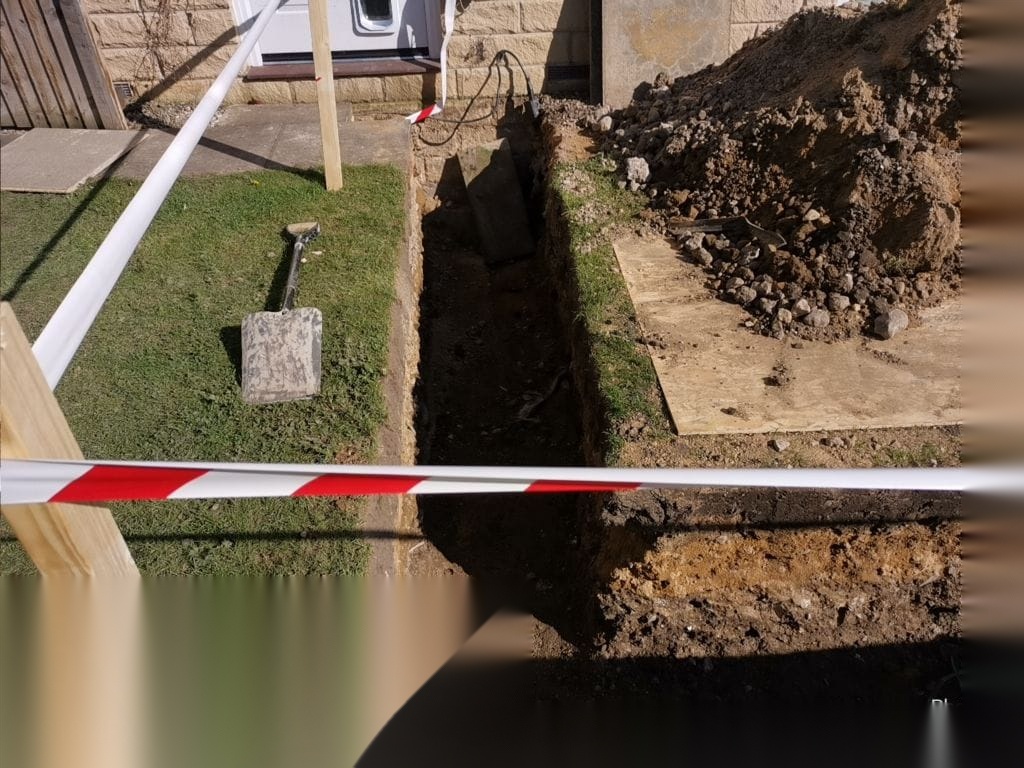 Narrow service trench excavated beside a lawn with spoil set aside during groundworks